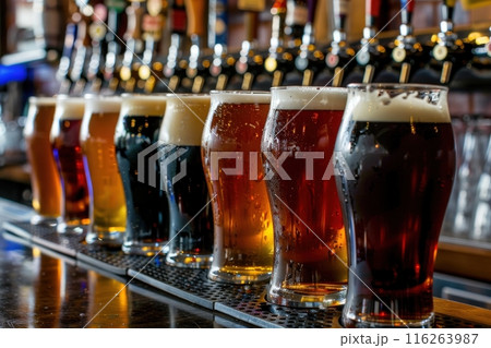 A row of beer glasses, each filled with a different type of brew, sits on a bar counter. 116263987