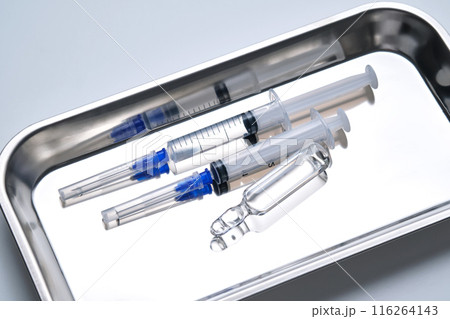Syringes with needles and an ampoule in a stainless steel medical tray. 116264143