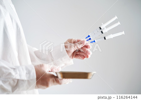 The doctor's hands in a white coat and gloves hold three syringes with medicine. The doctor's hands in a white coat and gloves hold three syringes with medicine. 116264144