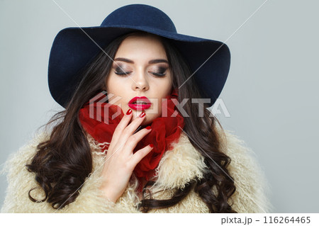 Lovely young brunette lady with makeup and long curly hair posing on blue background Lovely young brunette lady with makeup and long curly hair posing on blue background 116264465