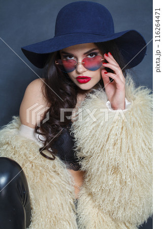 Young adult brunette lady with makeup and long curly hair posing on blue background Young adult brunette lady with makeup and long curly hair posing on blue background 116264471