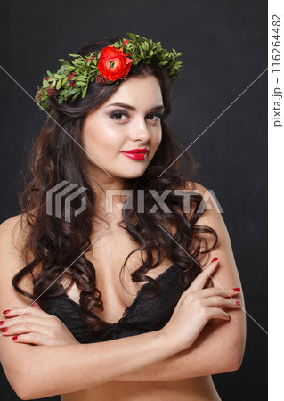 Happy young woman with floral head wreath looking at camera while standing against black background 116264482