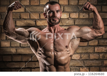 Bodybuilder showing his muscles against brick wall Bodybuilder showing his muscles against brick wall 116264680
