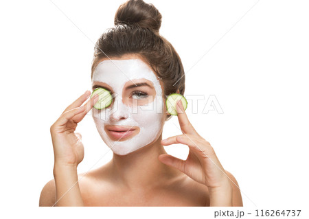 Woman with facial mask and cucumber slices in her hands 116264737
