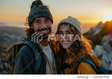 Caucasian couple hiking and wearing backpacks standing on mountain peak at sunset. 116265500
