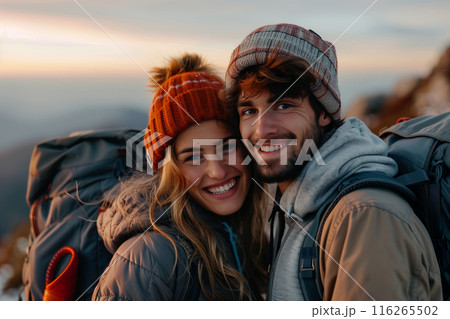 Caucasian couple hiking and wearing backpacks standing on mountain peak at sunset. Caucasian couple hiking and wearing backpacks standing on mountain peak at sunset. 116265502