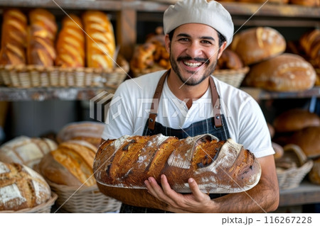 Smiling baker holding a large loaf of bread in a bakery. Studio portrait. 116267228