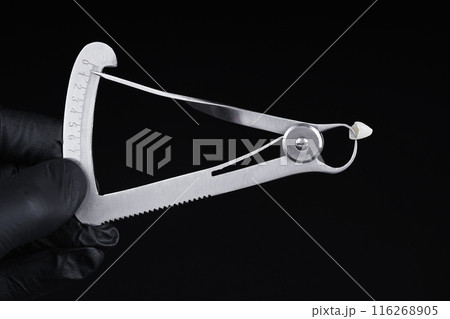 Micrometer measures the thickness of a high-quality zirconia crown. Black background. Micrometer measures the thickness of a high-quality zirconia crown. Black background. 116268905