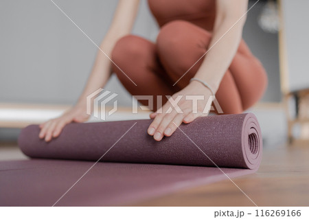 Woman trainer rolling out a mat after class. Rolled yoga mats in a studio create a peaceful atmosphere for meditation and exercise. Woman trainer rolling out a mat after class. Rolled yoga mats in a studio create a peaceful atmosphere for meditation and exercise. 116269166
