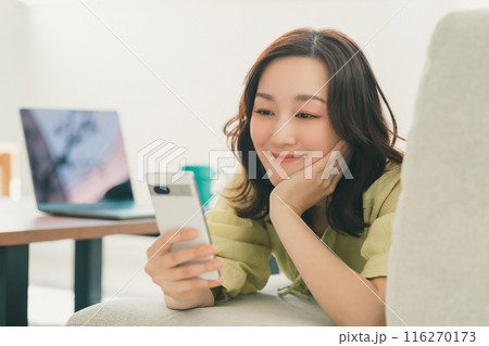 リビングのソファでスマホを操作する若い女性 116270173