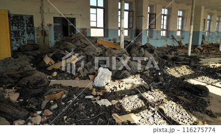 An abandoned, dilapidated building littered with piles of rubbish and bags of waste. Sunlight streams through the broken windows, illuminating the disorder and decay inside. 116275774
