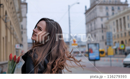 Portrait of a happy brunette girl with a tulip in the background of the city in the cold season. Portrait of a happy brunette girl with a tulip in the background of the city in the cold season. 116279393