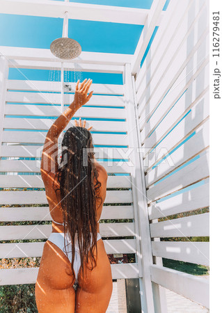 A woman in a bikini stands in front of a white shower stall. She is smiling and she is enjoying the moment. A woman in a bikini stands in front of a white shower stall. She is smiling and she is enjoying the moment. 116279481