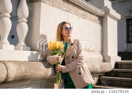 Woman holding yellow tulips, leaning against stone wall. Women's holiday concept, giving flowers. Woman holding yellow tulips, leaning against stone wall. Women's holiday concept, giving flowers. 116279534