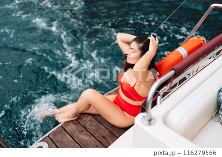 Yacht woman in a red bikini posing while on the bow of a yacht. Happy woman is sunbathing on the bow of a ship during a boat trip. Travel concept, vacation at sea 116279566