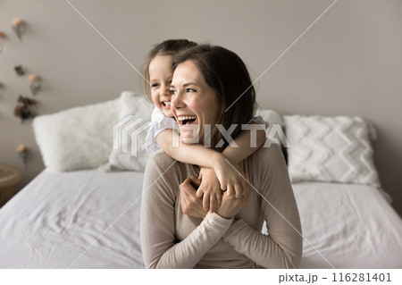 In cozy bedroom laughing awakened daughter cuddling from her mother In cozy bedroom laughing awakened daughter cuddling from her mother 116281401