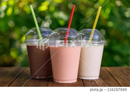 set of different delicious milkshakes in disposable plastic glasses with straw on table outdoors 116287889