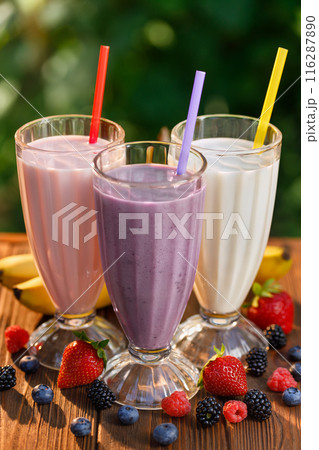 set of strawberry, banana and blueberry flavor milkshakes or smoothie in glasses on table outdoors set of strawberry, banana and blueberry flavor milkshakes or smoothie in glasses on table outdoors 116287890
