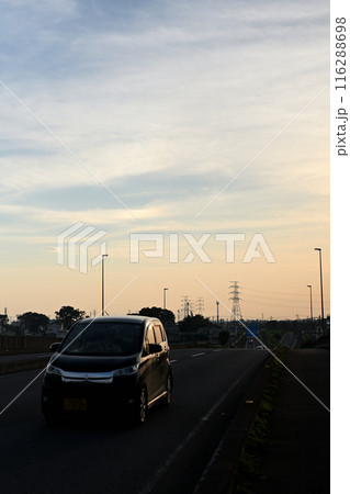 夕暮れの道を走ってゆく黒い車 116288698