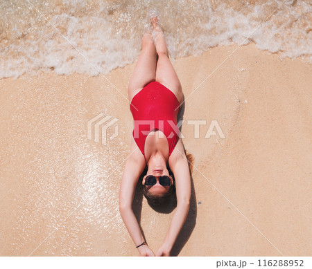 Young woman relaxing on sandy beach in red swimsuit. Top down view. Young woman relaxing on sandy beach in red swimsuit. Top down view. 116288952