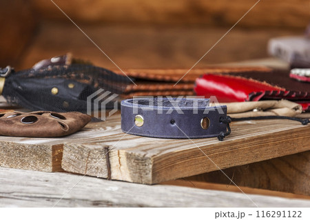 On the wooden surface lie handicrafts made of leather. Leather collar with metal rivets lies on a wooden surface On the wooden surface lie handicrafts made of leather. Leather collar with metal rivets lies on a wooden surface 116291122