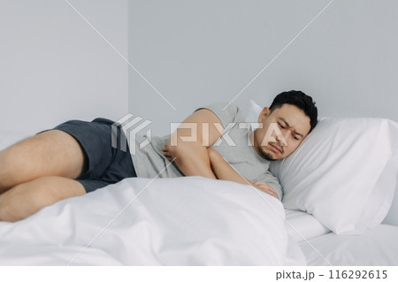 Serious and depressed man overthinking the problems lying on the bed. 116292615