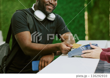 African American man tapping his golden credit card and smiling widely while female hand holding payment terminal 116292910