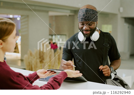 Positive African American man signing gym contract, female receptionist holding black clipboard carefully to help future gym resident Positive African American man signing gym contract, female receptionist holding black clipboard carefully to help future gym resident 116292940