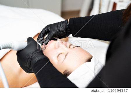 A close-up cosmetologist manipulates a hydropeeling machine to clean and rejuvenate a patient's skin in a modern clinic. A close-up cosmetologist manipulates a hydropeeling machine to clean and rejuvenate a patient's skin in a modern clinic. 116294587