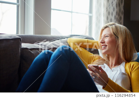 Happy, thinking and woman on couch, phone and rest in living room, morning and social media in house. Relax, calm and girl with mobile, smile and peace in lounge, cozy and person in apartment 116294854