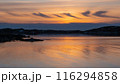 Serene sunset over a calm body of water, with the sky painted in warm hues of orange and yellow 116294858