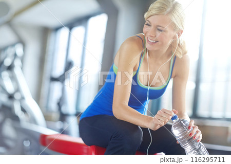Fitness, music and water with woman in gym for break, thinking about health, wellness or workout. Bottle, exercise and smile with happy young person at training center for physical improvement 116295711