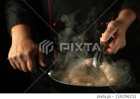 A cook turns a sausage with tongs in his hand while frying it in a frying pan. Low key concept of cooking sausage in the kitchen 116296232