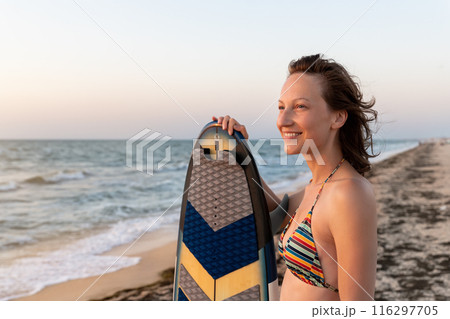 Portrait young adult slim sporty female surfer girl with surfboard silhouette stand at ocean coast wave against warm sunrise or sunset sun. Sport healthy carefree freedom lifestyle vacation concept 116297705