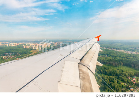 View of airplane wing, blue skies and green land during landing. Airplane window view. 116297893
