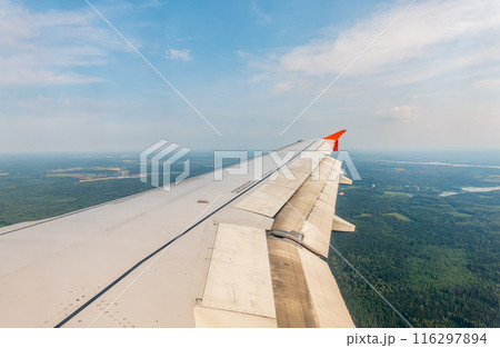 View of airplane wing, blue skies and green land during landing. Airplane window view. 116297894