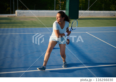 Female tennis player in action on blue outdoor court 116298830