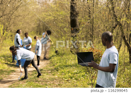 African american activist checks isolated mockup on laptop, participates in collecting rubbish from the forest area. Environmental volunteer works to protect the ecosystem, community outreach. 116299045