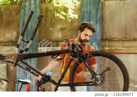 A fit young caucasian man repairs bike damage in home yard with professional repair-stand and tools. Dedicated athletic male engrossed in examining and fixing of modern bicycle outside with A fit young caucasian man repairs bike damage in home yard with professional repair-stand and tools. Dedicated athletic male engrossed in examining and fixing of modern bicycle outside with 116299077