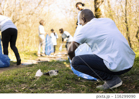 African american activist using disposal bags to recycle trash and plastic, collecting junk from the ground. Male environmentalist gathering litter, storing garbage in a trash bag, responsibility. African american activist using disposal bags to recycle trash and plastic, collecting junk from the ground. Male environmentalist gathering litter, storing garbage in a trash bag, responsibility. 116299090