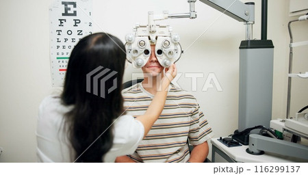Optometrist, man and phoropter for eye exam, vision and wellness in consultation room at hospital. People, doctor and help patient with machine, lens and assessment for healthy eyesight in clinic 116299137
