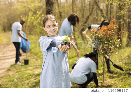 Little child volunteer holding small seedling tree in her hands, fighting to protect the environmental preservation and ecosystem. Young kid activist working to conserve nature and plant more trees. Little child volunteer holding small seedling tree in her hands, fighting to protect the environmental preservation and ecosystem. Young kid activist working to conserve nature and plant more trees. 116299157