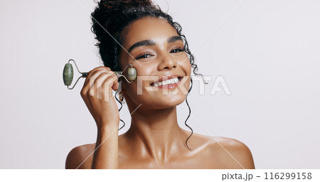 Face roller, smile and woman with cosmetics, skincare and makeup on grey studio background. Portrait, person and model with tool, wellness and treatment with beauty, dermatology and grooming routine 116299158