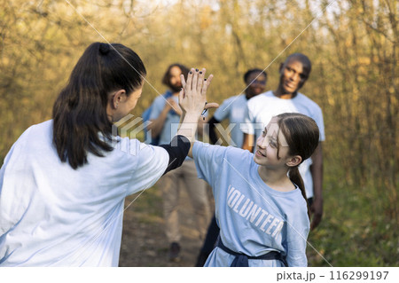 Cheerful woman doing high five with her daughter after finishing activity of clearing garbage and plastic waste, congratulating colleagues. Activist leader showing praise for a job well done. 116299197