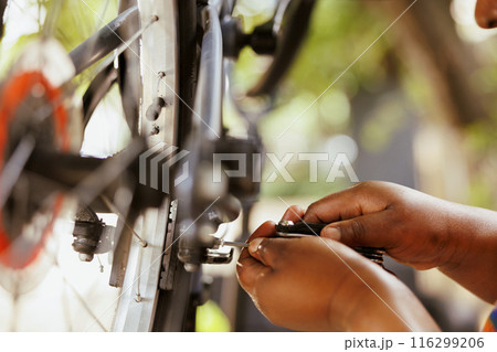 Detailed image of african american person's pair of hands doing maintenance on damaged bike tire rubber with specialized tool. Close-up shot of hand gripping screwdriver for tightening bicycle parts. 116299206