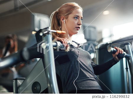 Gym, woman and concentrate on chest press machine for workout to exercise on health, fitness and muscles. Female person, earphones and music or audio for training, wellness and wellbeing or self care 116299832
