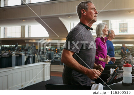 Running, gym or mature man on treadmill in workout or training for group class, health or cardio wellness. Runner, energy and male person on machine for fitness performance, challenge and exercise 116300539