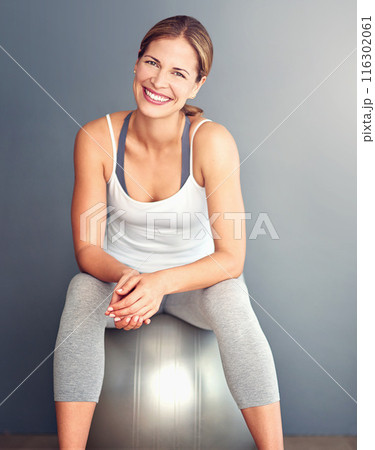 Exercise, portrait and sitting on ball with woman in studio on gray background for workout. Fitness, health or smile and happy person with equipment for physical improvement, training or wellness 116302061