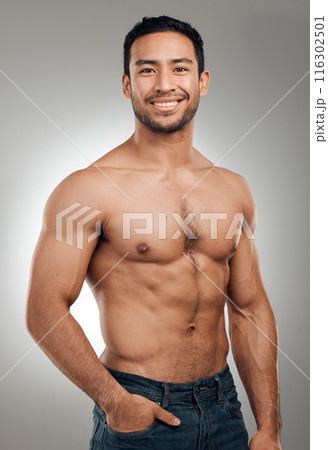 Man, portrait and happy in studio with abs or muscles, shirtless and grey background with model or bodybuilder. Jeans, strong chest and Asian male person on backdrop, confidence with six pack 116302501
