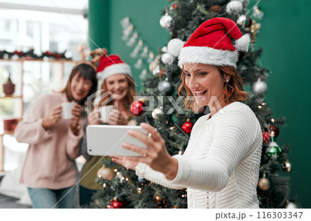 Woman, selfie and Christmas in living room for holiday, celebration and together with coffee. Technology, sisters and happy in family home for relax, vacation and drink in lounge for festive season 116303347